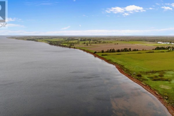Aerial view of a coastline with calm water, red soil, green fields, and distant trees. - Lot 6 Sonora Road, St  Peters Bay