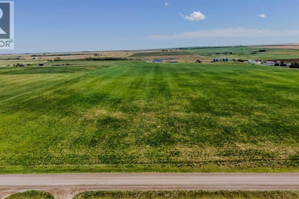 Wide shot of cultivated green fields with distant farm buildings and wind turbines on the horizon. - Lot 7, Magrath
