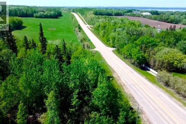 View of a paved road stretching uphill between dense green trees and utility poles on a sunny day. - Lot 72 Plan Laclabi, Lac La Biche