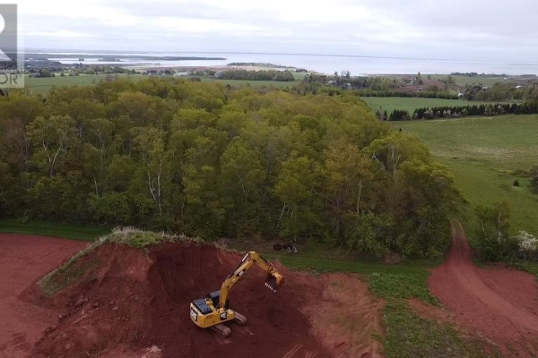 Aerial view of a construction site with an excavator, red soil, mature trees, green fields, and a distant coastline. - Lot 74 Newton Lane, Stratford
