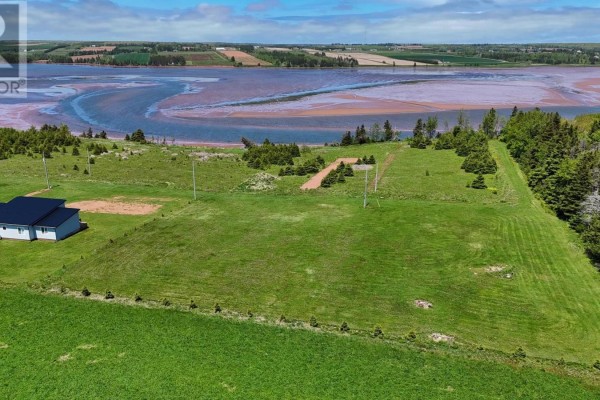 Drone view of a cleared grassy lot with a small house on the left, overlooking a bay under a blue sky. - Lot Aitken Lane, Bay Fortune