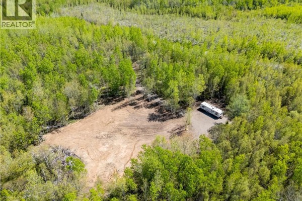 Aerial view of a large wooded lot with a travel trailer parked on a gravel clearing. - Lot Duguay Point Road, Shemogue