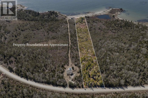 View of a small dark blue shed on a sandy beach with wooded trees and calm ocean. - Lot Mb-1 Rockland Road, East Side Of Ragged Island