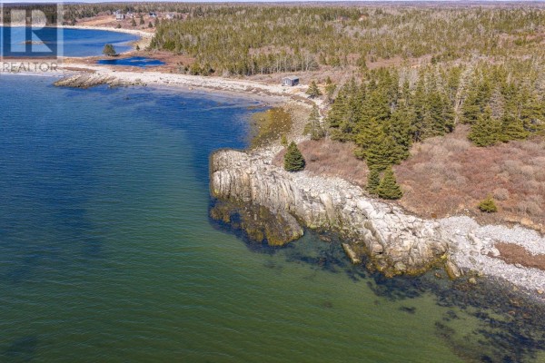 Rocky coastline with trees and calm blue water, showing the edge of the property. - Lot Mb-4 Rockland Road, East Side Of Ragged Island