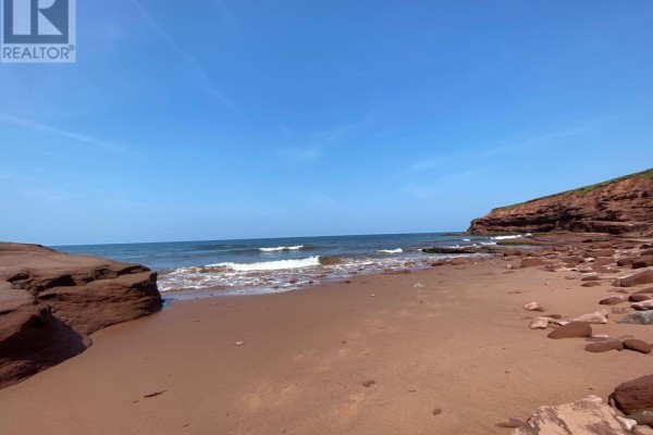 A red sandy beach with gentle waves lapping the shore and large sandstone formations. - Lot Park Corner Lane, Park Corner