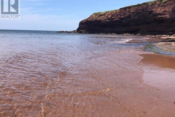 Clear, shallow water with a sandy bottom showing ripples and a red sandstone cliff above. - Lot Park Corner Lane, Park Corner