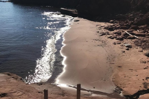 Sunlight sparkles on the water's edge as waves wash onto a sandy cove with rocky cliffs. - Lot Park Corner Lane, Park Corner