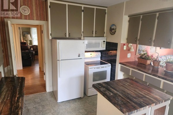 Kitchen with white appliances, dark countertops, and cabinets, looking into the living area. - Lots 3&10, 70 Victoria Road, Lunenburg