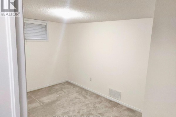 Empty carpeted basement room with a window and beige walls. - Lower - 11 Catherine Drive, Barrie