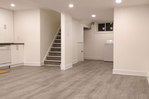 Basement area with gray flooring, white walls, stairs, and laundry appliances. - Lower - 1185 Woodbine Avenue, Toronto