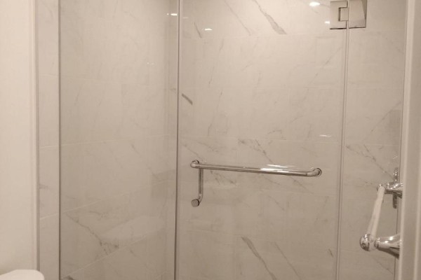 Close-up of a modern bathroom's glass shower stall with marble-look tile and chrome fixtures. - Lower - 1185 Woodbine Avenue, Toronto