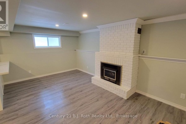 Basement living area with light green walls, a white brick fireplace, and grey wood-look flooring. - Lower - 12 Shannon Street, Orillia