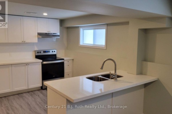 L-shaped kitchen with white cabinets, stainless steel appliances, a breakfast bar, and grey flooring. - Lower - 12 Shannon Street, Orillia