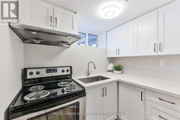 Kitchen with white cabinets, stainless steel stove, and sink under a small window. - Lower - 123 Bowman Avenue, Whitby