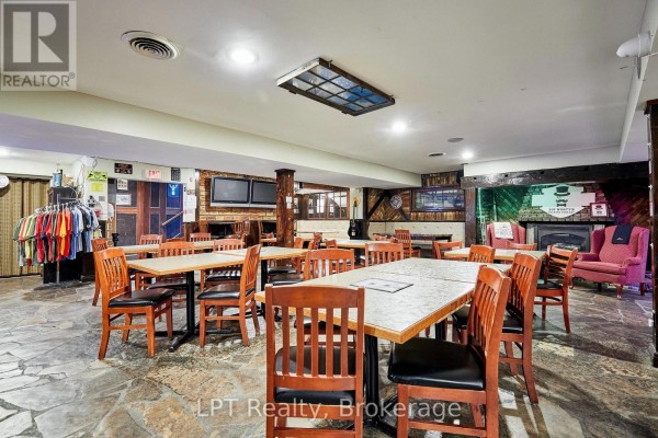 Dining area with wooden tables and chairs in front of a stone fireplace and bar. - Lower - 1540 Highway 2 Highway, Clarington