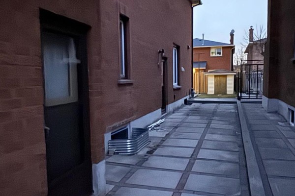 View of a concrete walkway beside a brick house with window wells and a small shed. - Lower - 162 Jackman Crescent, Vaughan