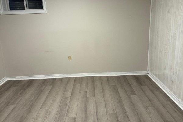 Empty room with light beige walls, wood-look laminate flooring, and white baseboards. - Lower - 162 Jackman Crescent, Vaughan