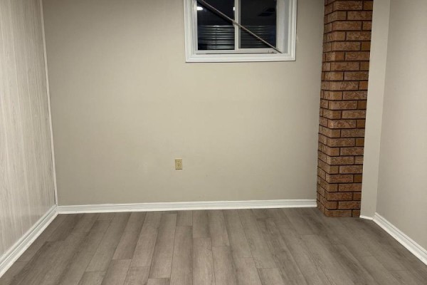 Room with light beige walls, wood-look laminate flooring, white baseboards, and a brick column. - Lower - 162 Jackman Crescent, Vaughan