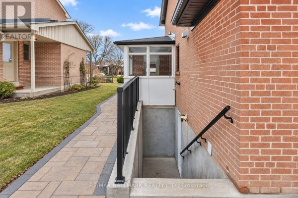Exterior basement entrance with concrete stairs and metal railing, next to brick wall. - Lower - 18 Aldenham Crescent, Toronto