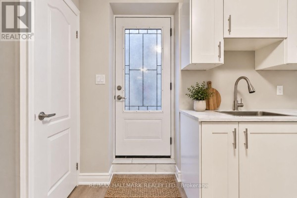 Small kitchen area with white cabinets, stainless steel sink, and frosted glass door. - Lower - 18 Aldenham Crescent, Toronto