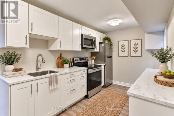 Compact kitchen with white shaker cabinets, stainless steel appliances, and light wood flooring. - Lower - 18 Aldenham Crescent, Toronto