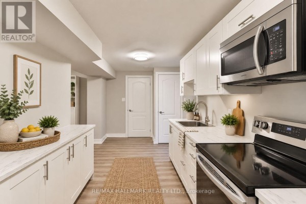 L-shaped kitchen with white cabinets, stainless steel appliances, and marble-look countertops. - Lower - 18 Aldenham Crescent, Toronto