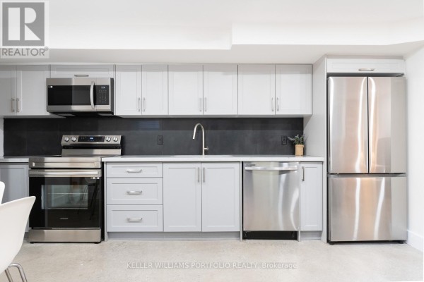 Modern kitchen with light grey cabinets, stainless steel appliances, and dark backsplash. - Lower - 180 Maria Street, Toronto