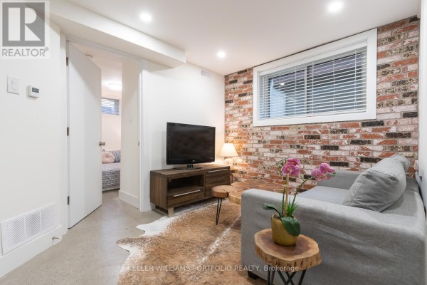 Living area with sofa and exposed brick accent wall, open to hallway. - Lower - 180 Maria Street, Toronto