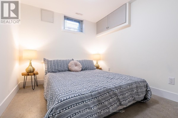 Bedroom with a queen-size bed, patterned bedding, and two bedside tables with lamps. - Lower - 180 Maria Street, Toronto