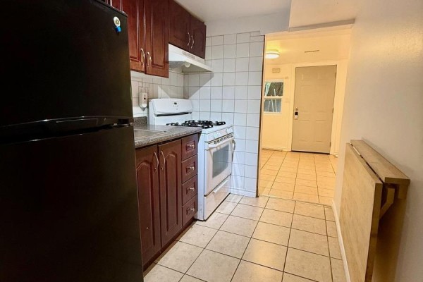 Kitchen with dark cherry cabinets, granite counters, white appliances, and an open doorway to another room. - Lower - 191 Coxwell Avenue, Toronto