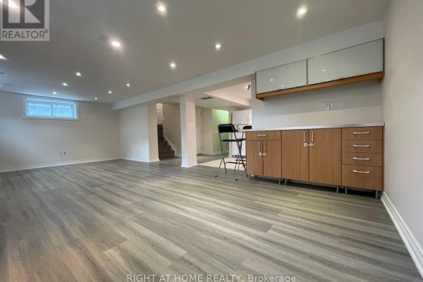 Finished basement with kitchenette, grey vinyl flooring, and wooden cabinets. - Lower - 191 Princess Avenue, Toronto
