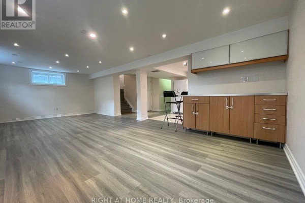 Finished basement with kitchenette, bar stools, and wood-look vinyl flooring. - Lower - 191 Princess Avenue, Toronto