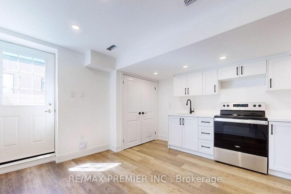 Basement kitchen with white cabinets, stainless steel stove, sink, and door to outside. - Lower - 208 Mcroberts Avenue W, Toronto