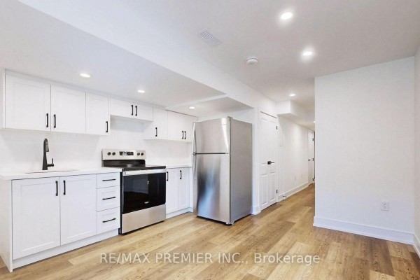 Basement kitchen and hallway with white cabinets, stainless steel refrigerator, and light wood floor. - Lower - 208 Mcroberts Avenue W, Toronto