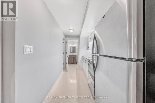 View down a hallway showing a stainless steel refrigerator and a doorway. - Lower - 223 Landsbridge Street, Caledon