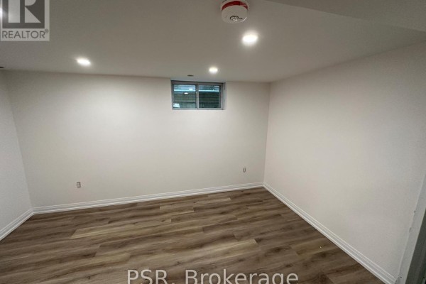 Empty room with white walls, wood-look flooring, and a small window near the ceiling. - Lower - 25 Coulson Avenue, Toronto