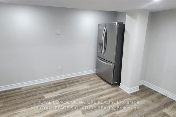 Empty room with light grey walls, light wood-look laminate flooring, and a stainless steel refrigerator. - Lower - 25 Lyle Drive, Clarington