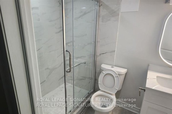 Bathroom with a glass-enclosed shower, marble-look tiles, white toilet, and vanity with sink. - Lower - 25 Lyle Drive, Clarington