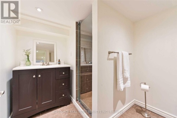 A bathroom vanity with a dark wood cabinet and white countertop, and a glass-enclosed shower. - Lower - 25 Mann Avenue, Toronto