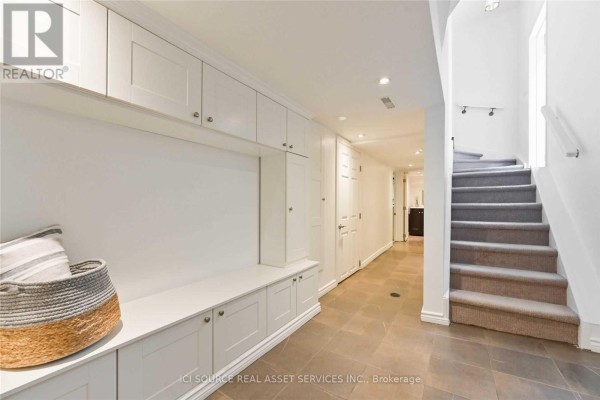A long hallway with beige built-in storage units, a bench, a staircase, and stone tile flooring. - Lower - 25 Mann Avenue, Toronto
