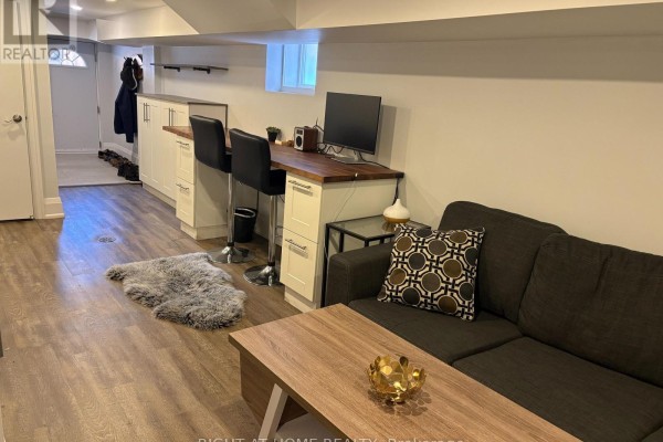 Living area with a charcoal sofa, coffee table, desk with computer, and bar seating. - Lower - 39 Amherst Avenue, Toronto