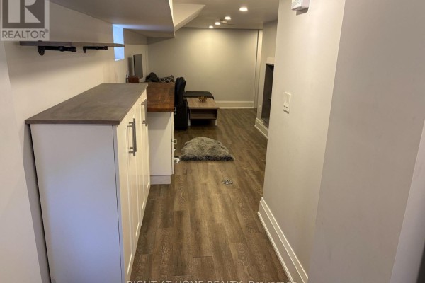 View from the hallway looking towards the living room and a kitchenette with white cabinets. - Lower - 39 Amherst Avenue, Toronto