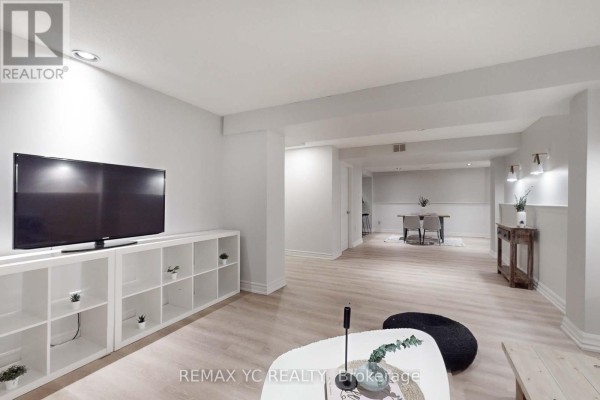 Open concept living area with a television on a white shelving unit and a dining area beyond. - Lower - 4 Theobalds Circle, Richmond Hill