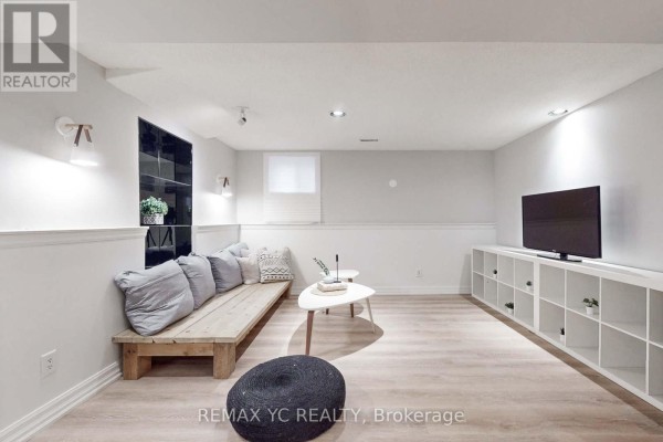 Living area with a wooden bench couch, coffee tables, and a television on a white shelving unit. - Lower - 4 Theobalds Circle, Richmond Hill
