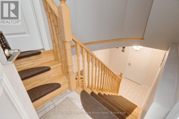View looking down a wooden staircase with brown carpet treads and a white door below. - Lower - 41 Greenview Circle, Vaughan