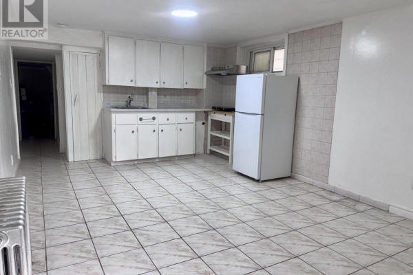 Basement kitchen with white cabinets, dual-tone tiled floor, refrigerator, and stainless steel range hood. - Lower - 415 Delaware Avenue, Toronto
