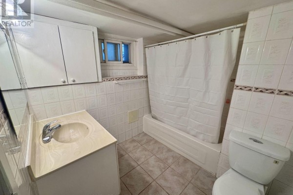 Small bathroom with a vanity, sink, toilet, bathtub, and tiled walls and floor. - Lower - 415 Delaware Avenue, Toronto