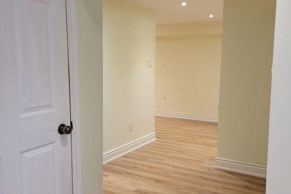 Empty room with light yellow walls, baseboards, and light wood laminate flooring. - Lower - 42 Ambleside Crescent, Markham