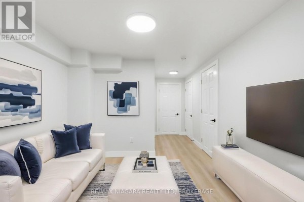 Living room with a white sectional sofa, ottoman coffee table, modern abstract art, and a television on a console. - Lower - 422 Brunswick Street, Hamilton