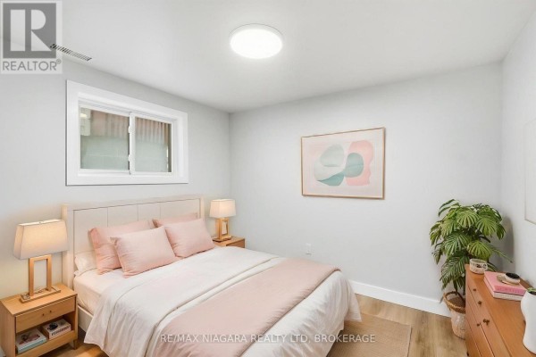 Bedroom with a queen-sized bed, pink bedding, wooden bedside tables, dresser, and a small horizontal window. - Lower - 422 Brunswick Street, Hamilton